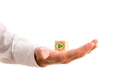 Green arrow icon in a circle pointing to the right of the frame on a wooden cube in a mans hand in a conceptual image, isolated on white with copyspace.の写真素材