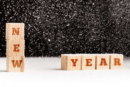 Generic undated New Year winter background with falling snowflakes covering rows of wooden alphabet blocks spelling the words New Year over a dark background with copyspace.の写真素材