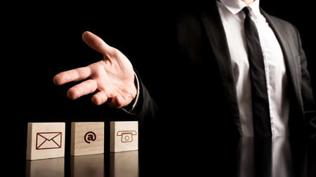 Businessman Showing Contact Icons on Small Wooden Pieces on Table. Isolated on Black Background.の写真素材