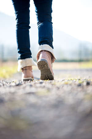 Feet of a woman in jeans and boots walking along a rural path away from the camera.の写真素材