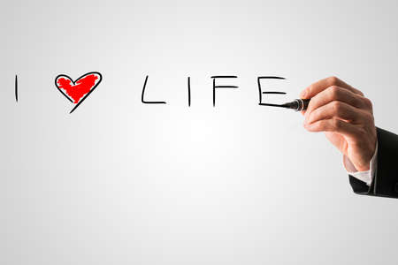 Man writing a message I love life with a red heart on a virtual interface over grey in a motivational message.の写真素材