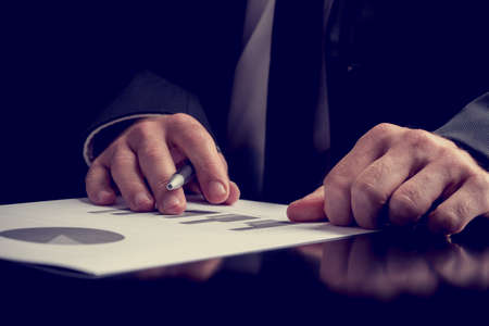 Businessman working on a presentation or performance analysis making notes on a set of bar and pie graphs, close up view of his hands as he sits at a desk.の写真素材
