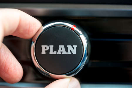 Close up of the fingers of a man turning on a plan button with the word - Plan - in white lettering on a piece of electronic equipment.の写真素材