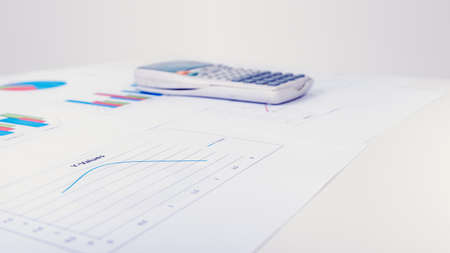 Desk calculator next to printed business documents with different diagrams as line, pie or columns charts, concept of financial analysis and data representation.の写真素材