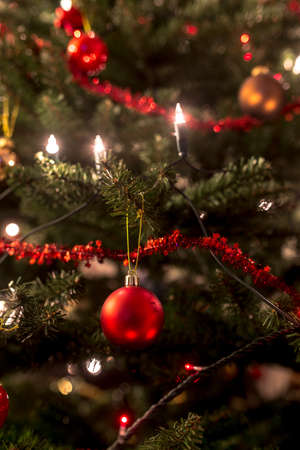 Festive Christmas tree decorated with traditional ornaments as lights, red baubles and tinsel,...