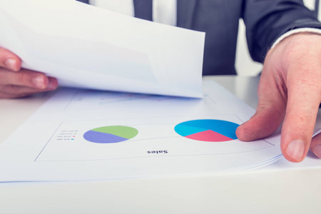 Retro image of the hands of a businessman analysing a set of pie graphs and holding a spreadsheet...