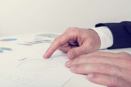 Retro image of businessman analysing printed business documents as he sits at his white desk...