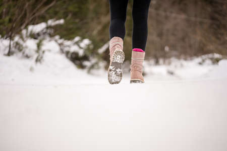 Person walking away from the camera through white winter snow wearing boots in the countryside, low angle view of the lower leg with copyspace in the foreground.の写真素材