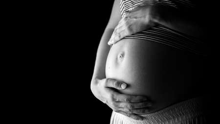 Image of pregnant woman holding her pregnant belly over black background.の写真素材