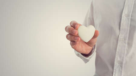 Retro image of a man holding a white heart. Concept of Valentines, love or romance, with copyspace to the left.の写真素材