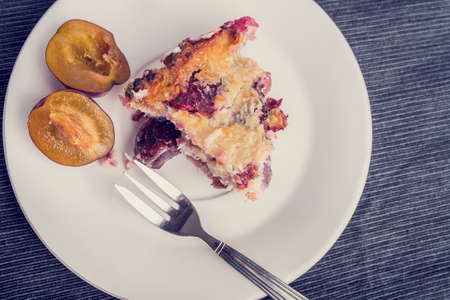 Top view of home baked plum pie served on a plate for dessert with a halved fresh plum alongside....