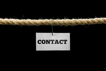 White card with Contact text hanging by wire from a rope isolated on black background with copyspace.の写真素材
