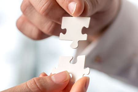 Two businesspeople fitting together matching interlocking puzzle pieces conceptual of teamwork and...