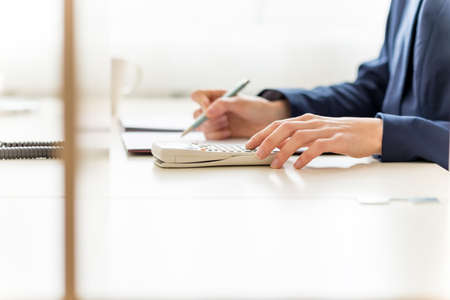 View of the arms of a businesswoman sitting working at her desk in the office checking and analysing...
