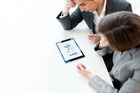 Overhead view of two business colleagues, a man and woman, analysing a statistical business graph on...