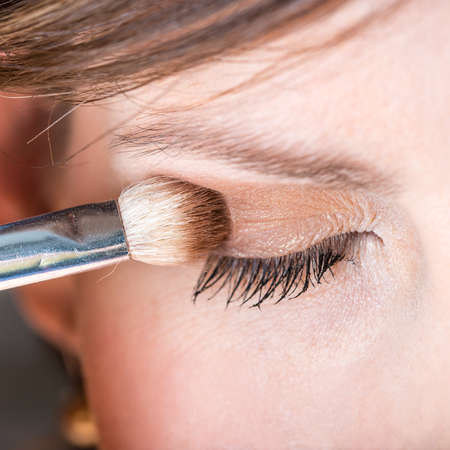 Fashion and beauty concept of a woman applying eye shadow to her eyelid with an applicator, closeup detail of one eye.の写真素材
