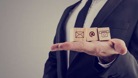 Retro style image of a businessman holding three wooden cubes with contact symbols - envelope, at sign and telephone - conceptual of communication and business support.