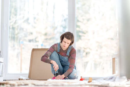 Young woman doing DIY repairs at home putting together self assembly furniture using a screwdriver.の写真素材
