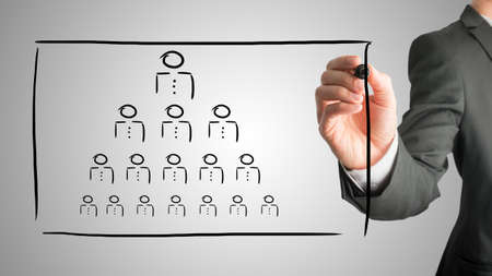 Businessman drawing a hierarchy concept on a virtual interface with a pyramid formation of people...