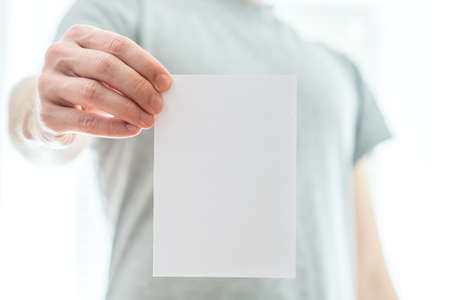 Man in a grey t-shirt holding a blank white piece of paper in his extended hand with copyspace for your text or advertisement.の写真素材