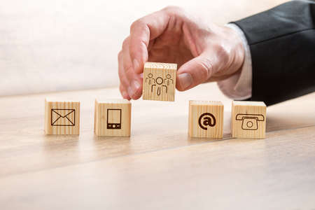 Close up Businessman Arranging Wooden Cubes with Contact and Customer Care Symbols on Top of a Table.の写真素材