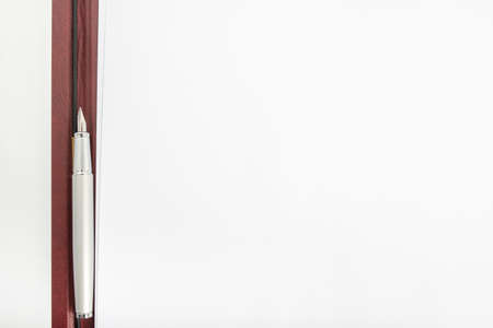 Top view of a pen lying in between two blank sheets of paper in an opened leather folder.の写真素材