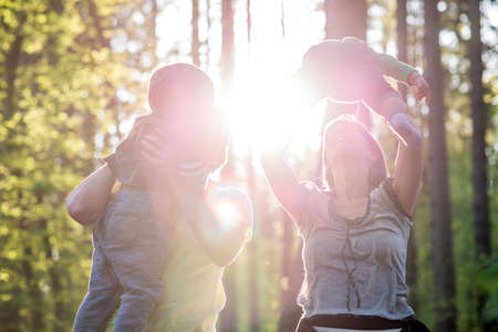 Mother and Father Lifting Children into the Air While Walking in Forest with Bright Sunlight Behind Them.の写真素材