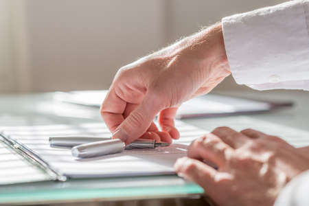 Close up view of the hand of a businessman reaching for his fountain pen lying on top of paperwork...