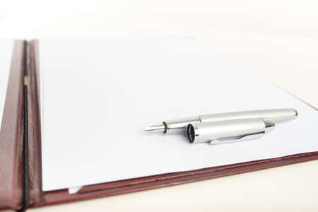 Low angle view of a stylish metallic fountain pen lying on blank paper on a folder or clipboard, with copyspace.の写真素材