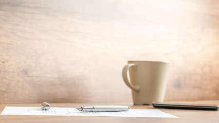 Fountain pen lying on office paperwork alongside a mug of coffee viewed low angle against a rustic or vintage style wall with copyspace.の写真素材