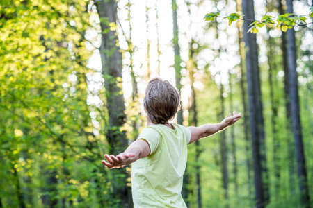 Young man celebrating nature standing in woodland with outspread arms facing the glowing morning sun...