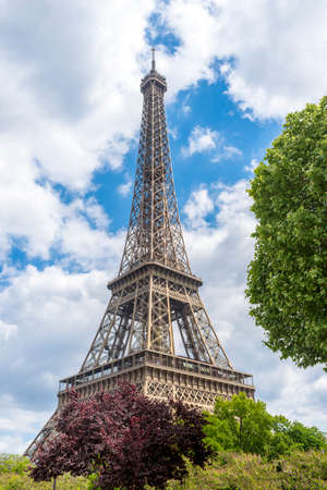 Eiffel Tower and tree twigs with blue sky and white clouds, Paris, France.
