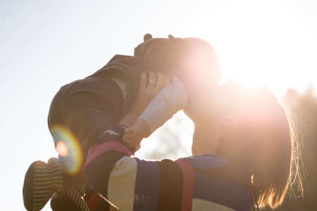 Woman Lifting and Kissing Baby Backlit by Bright Sunlight Outdoors in Family, Love and Togetherness...