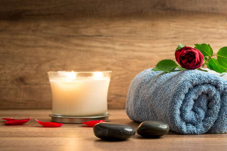 Romantic spa arrangement with a burning white scented candle, red petals, two black stones and a rose on a blue folded soft towel.の写真素材