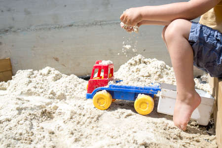 Young Boy Playing with his Plastic Truck Toy on White Sand at the Beach Under the Heat of the Sun During Summer.の写真素材