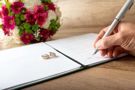 Man signing a marriage register as a groom or witness with a stylish fountain pen with two wedding...