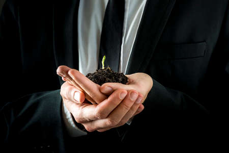 Conceptual Businessman in Black Suit, Holding a Conceptual Soil with Fresh Young Sprout with his both Hands.の写真素材