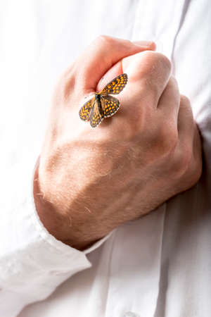 Man with a butterfly with open wings on his clenched hand which he is holding to his chest in a...