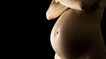 Miracle of life concept - closeup of a bare pregnant belly in a late stage of pregnancy. Isolated over black background.の写真素材