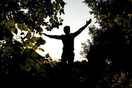 Silhouette of a Happy Young Man Opening his Arms for Happiness While Standing at the Fields with Trees.の写真素材