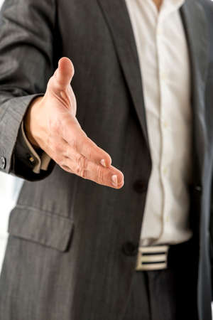 Close up Young Businessman in Black Suit Offering you a Hand in Handshake Gesture at the Camera.