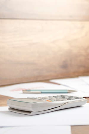 White plastic desk calculator on a printed document, work papers  or assignment, on a wooden desk or workspace, close-up. Suitable for business, accounting, education or science  and research concept.の写真素材