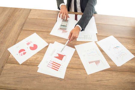 Businessman giving a presentation with assorted analytical graphs and charts spread out on the desk in front of him pointing to relevant information with a pen.の写真素材