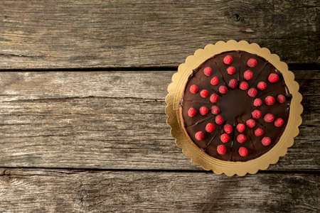 Top view of delicious chocolate cake decorated with juicy fresh raspberries on old textured wooden desk with plenty of copy space on the left side.の写真素材