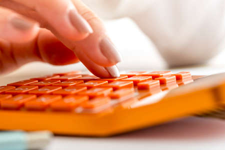 Closeup of female accountant or banker making calculations on orange desk calculator.の写真素材