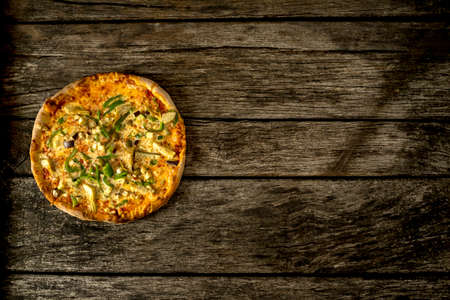 Top view of delicious freshly baked vegetarian pizza topped with eggplant, green  peppers and anchovies, lying to the left side on old textured rustic wooden board with copyspace.の写真素材