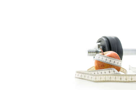Close up of waist measuring tape wrapped around red apple on white background, part of black and silver dumbell visible in background.の写真素材