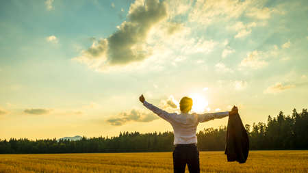 Young ambitious executive enjoying and celebrating his business success as he stands in beautiful nature under majestic sky with his arms spread widely holding his thumbs up.の写真素材