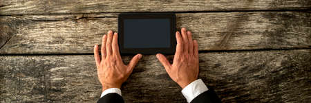 Top view of businessman hands holding black digital tablet on textured antique wooden desk.の写真素材