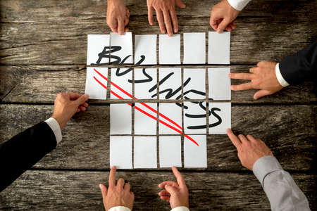 Business planning and strategy concept with a team of businessmen each inputting blank white cards into a grid on a table for a composite with the word Business, view from overhead.の写真素材